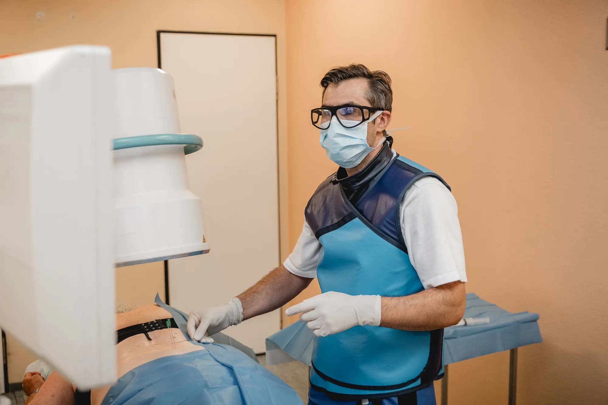 Arzt mit Mundschutz und Röntgenschutzweste bereitet einen Eingriff an einem Patienten vor.