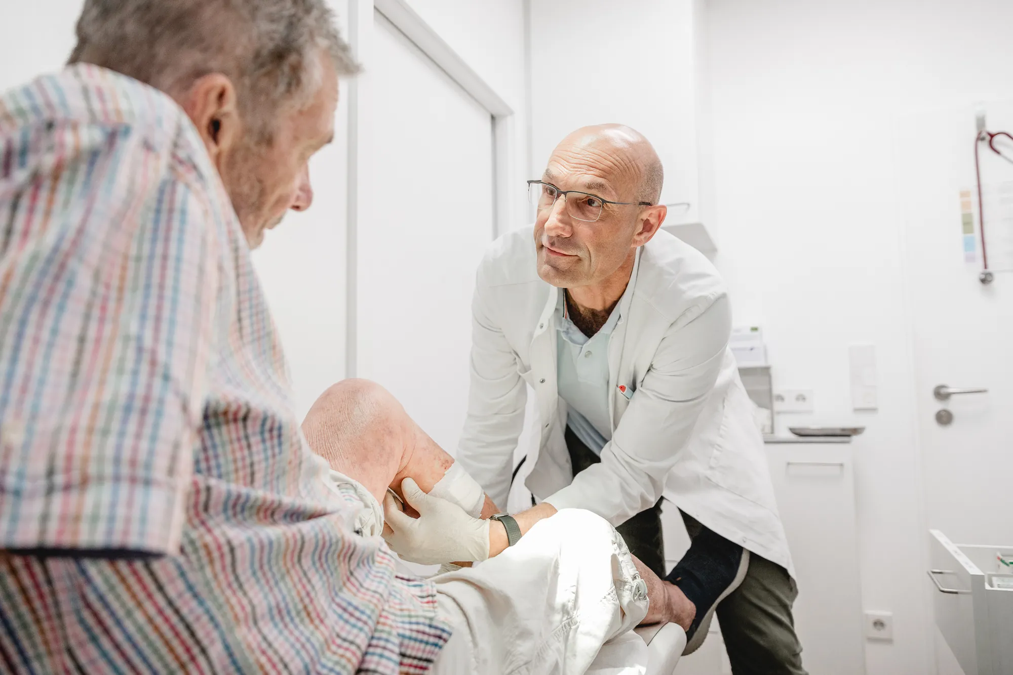 Arzt im weißen Kittel untersucht das Knie eines älteren Patienten.