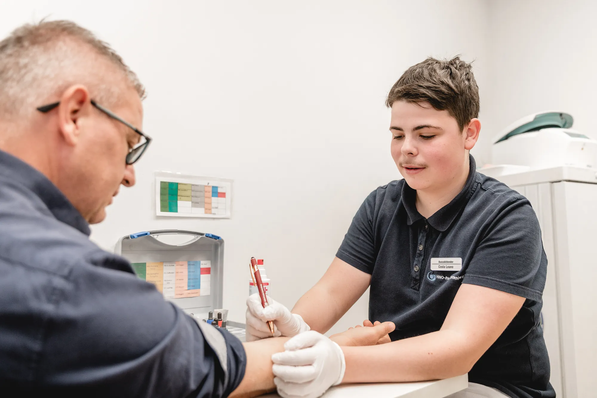 MFA nimmt einem Patienten mit einer Stechhilfe Blut an der Fingerkuppe ab.