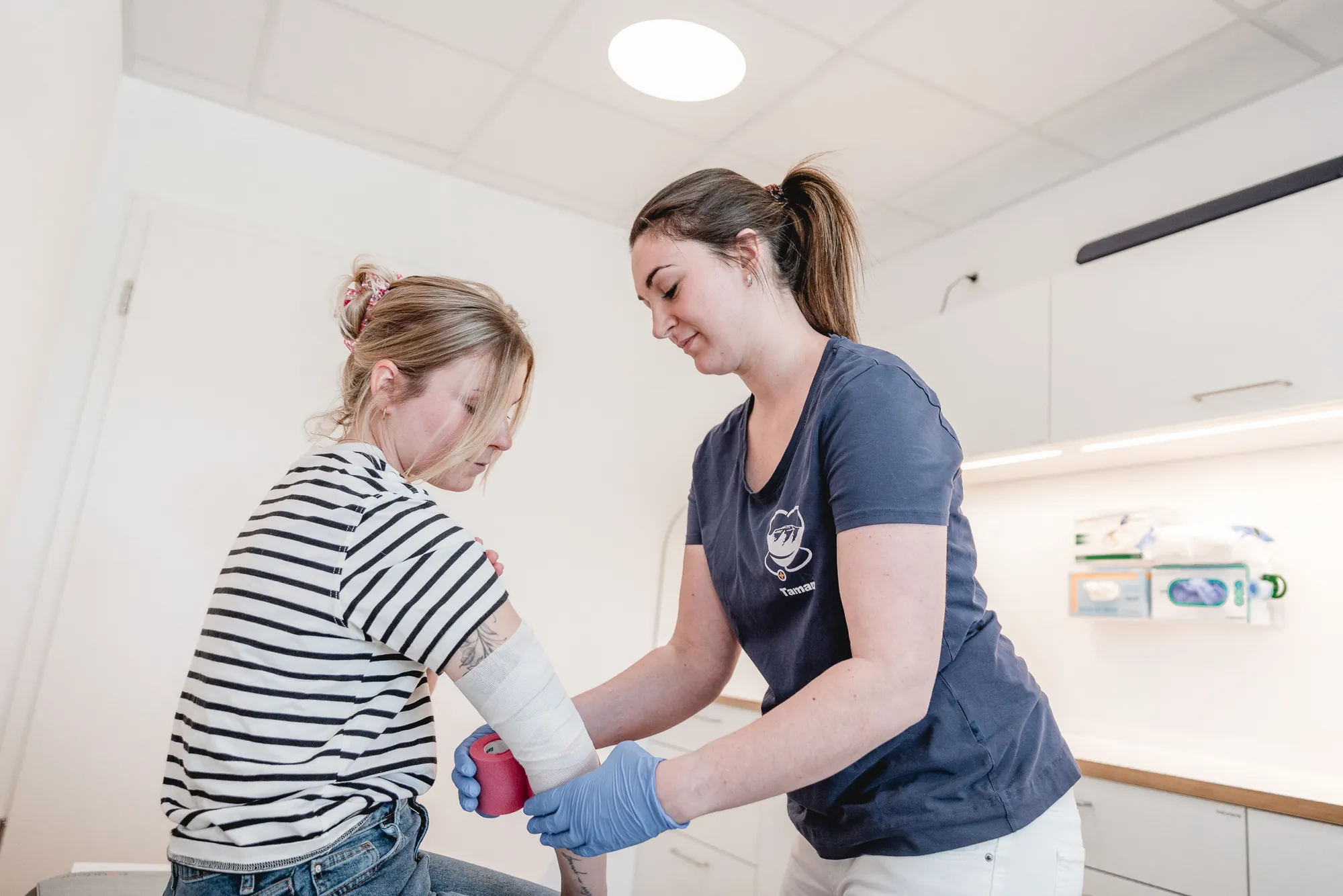MFA legt einer Patientin einen Verband am Unterarm an.
