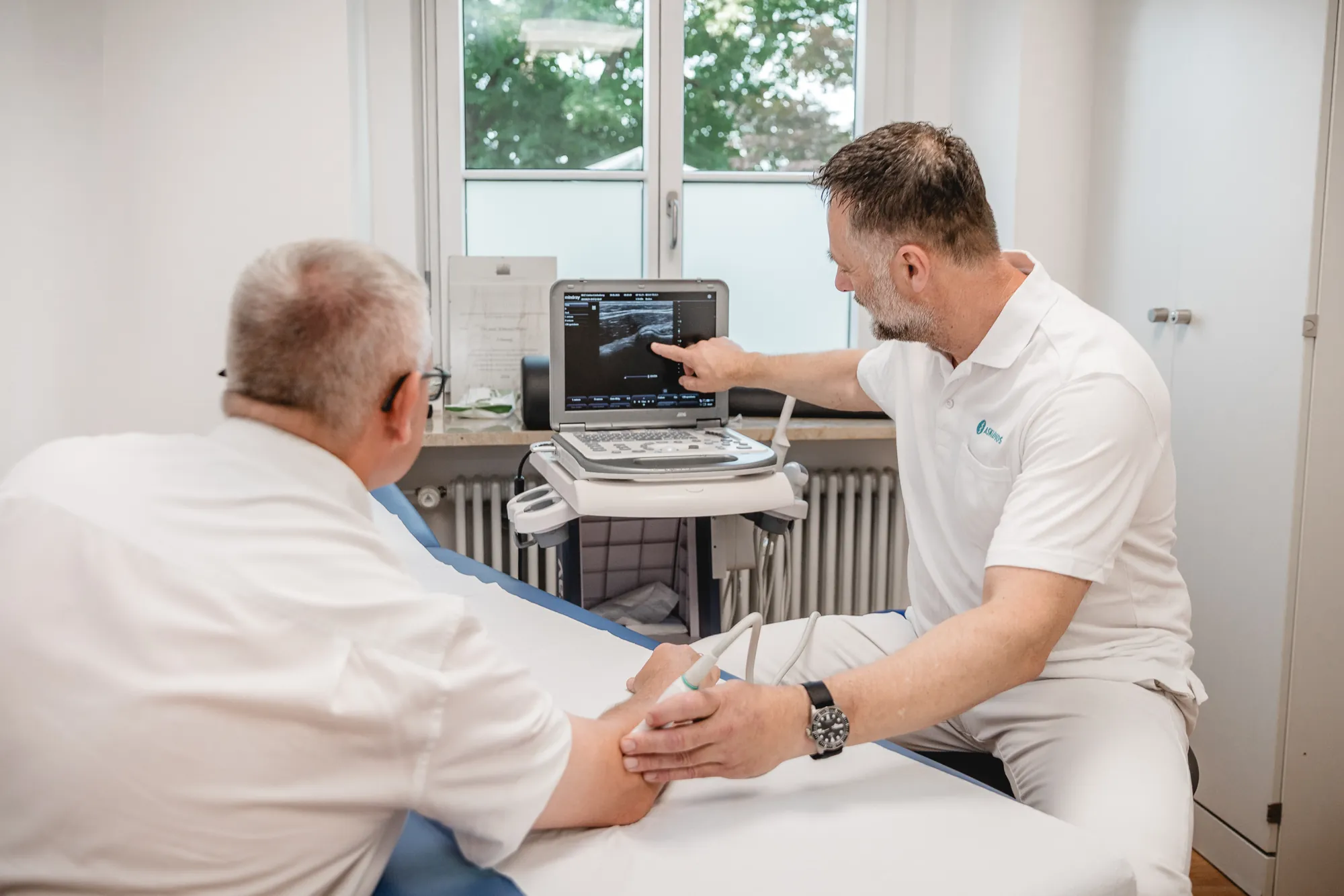 Arzt zeigt einem Patienten während der Ultraschalluntersuchung das Bild auf dem Monitor.