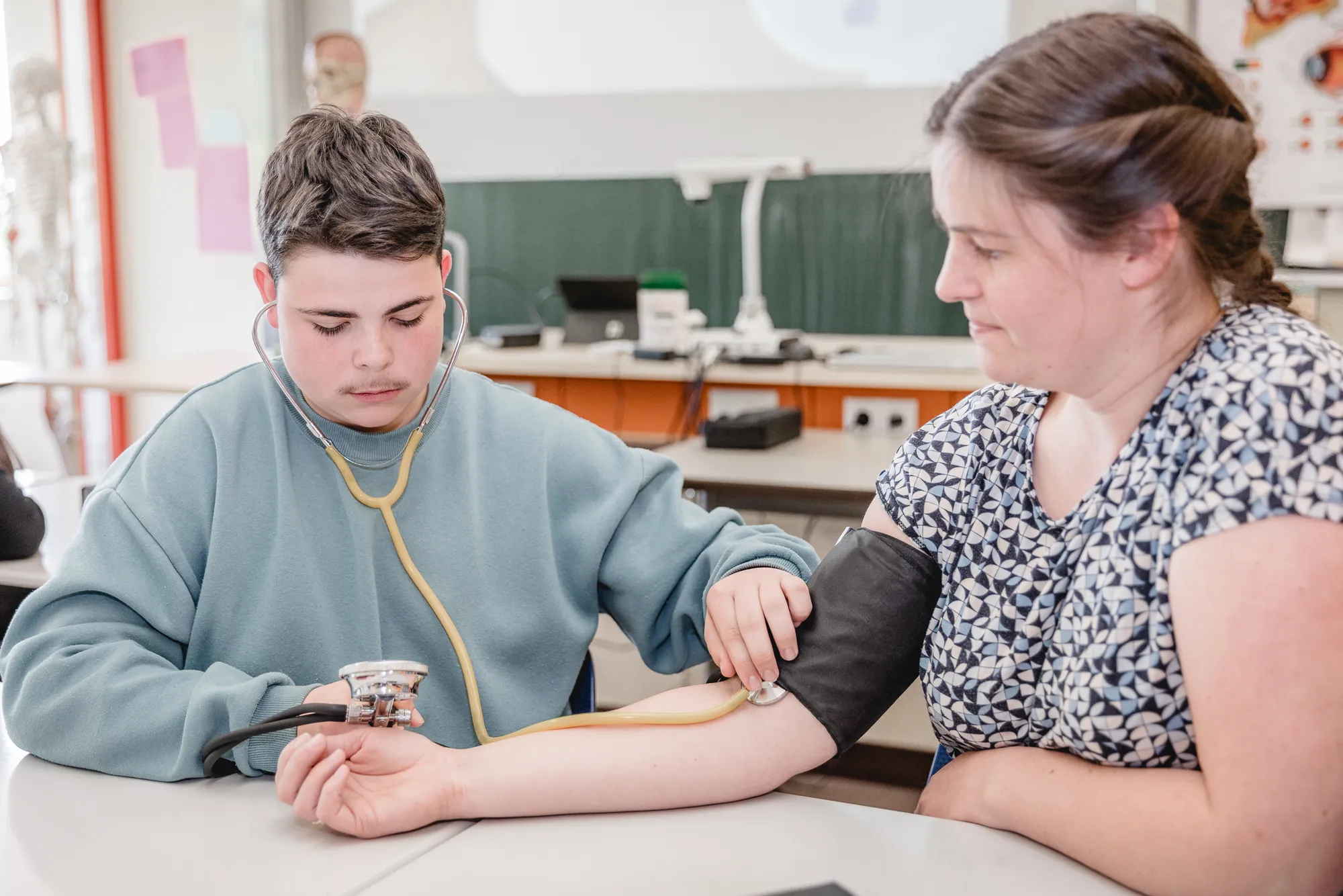 Schüler misst im Unterricht mit Stethoskop und Manschette den Blutdruck am Arm seines Gegenübers.